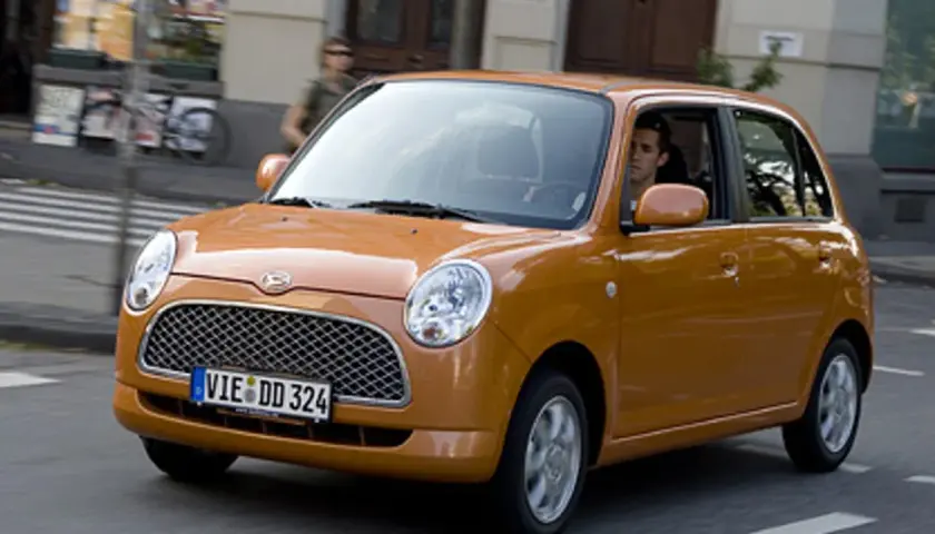 Pomarańczowy Daihatsu Trevis z kierowcą za kierownicą jedzie ulicą.