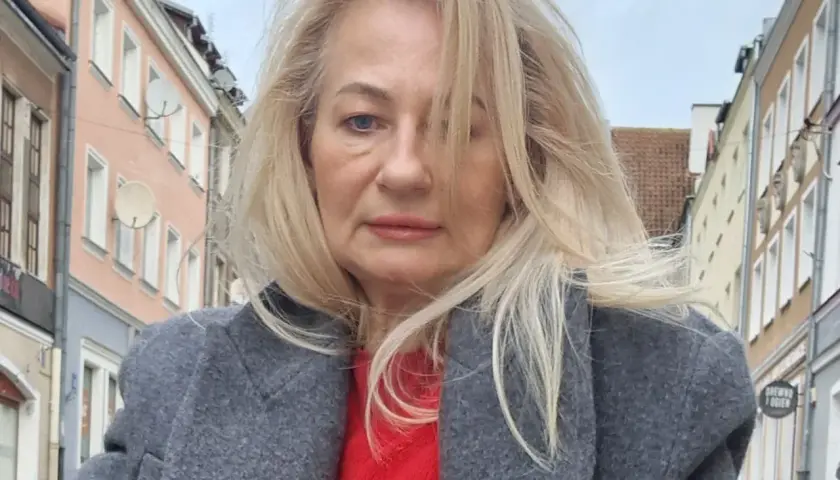 Szafiarka Dorka, ile ma lat? Kobieta w szarym płaszczu i czerwonym swetrze na tle kamienic.