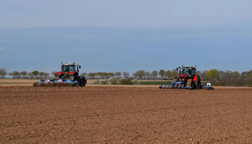 Deux tracteurs préparent le sol pour la culture du lin. Le champ est labouré, prêt pour les semis.