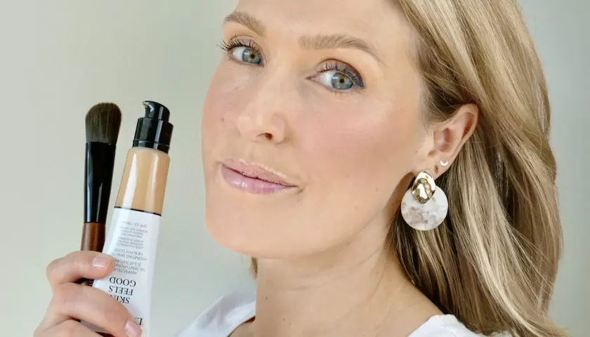 En kvinna håller upp en flaska Giorgio Armani foundation och en borste. Hennes hud ser naturligt fräsch ut.