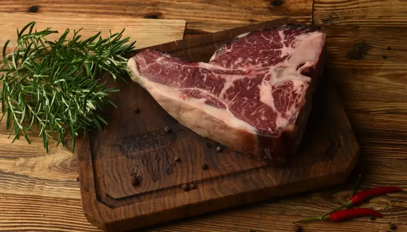 Surowy stek na desce z rozmarynem i pieprzem. Sezonowanie wołowiny na mokro vs na sucho kluczowe różnice w smaku.