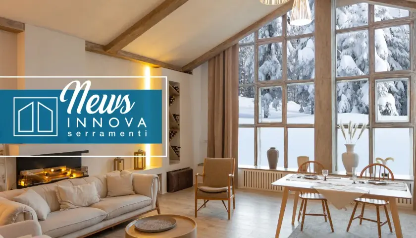Interno accogliente con camino e divano, affacciato su un paesaggio innevato attraverso ampie finestre baita montagna.