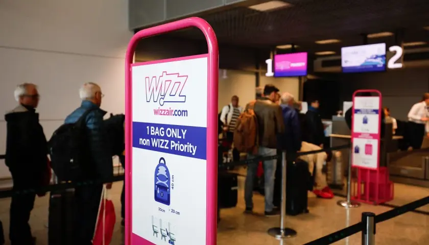 Tablica Wizzair z zasadami bagażu podręcznego, w tle kolejka pasażerów do odprawy.