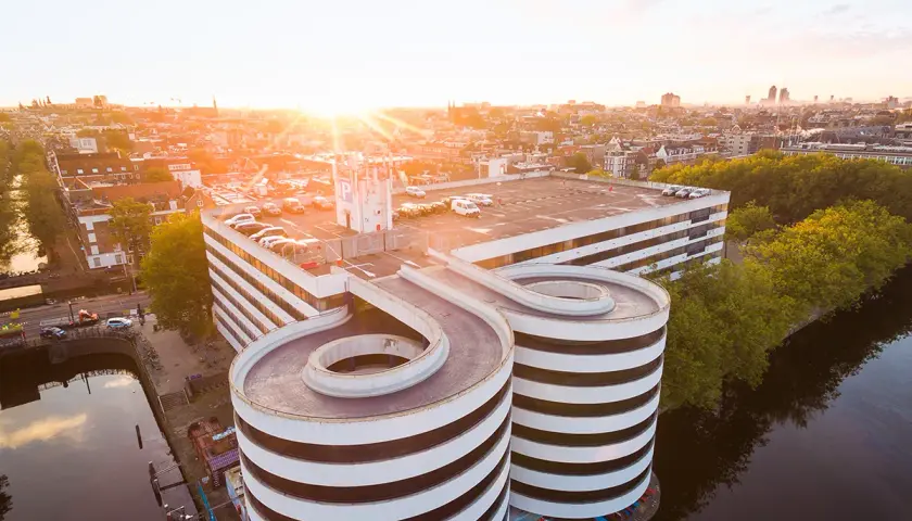 Sonnenuntergang über Amsterdam. Ein Parkhaus mit spiralförmigen Rampen ragt über den Kanal.