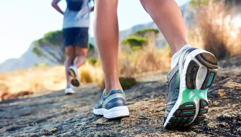 Dwie osoby biegną po kamienistej ścieżce. Zbliżenie na buty biegowe, które są kluczowe, jak przygotować się do biegu na 10 km.
