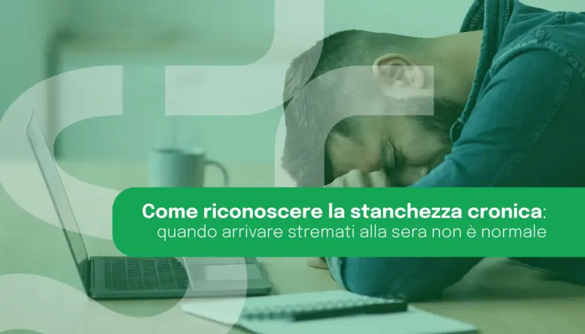 Uomo esausto appoggiato alla mano, con laptop e taccuino. La stanchezza cronica può manifestarsi anche con un senso di spossatezza serale.