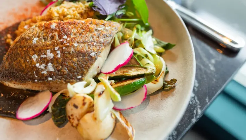 Delicioso pescado blanco crujiente con guarnición de verduras a la parrilla y rábano fresco.