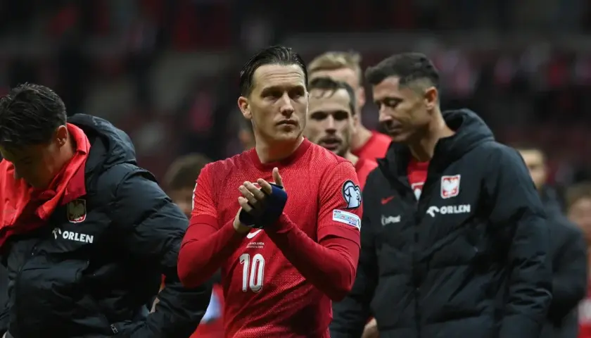 Piłkarze reprezentacji Polski, w tym Lewandowski, w czerwonych strojach i czarnych kurtkach, oklaskują kibiców. Duma z barw narodowych.