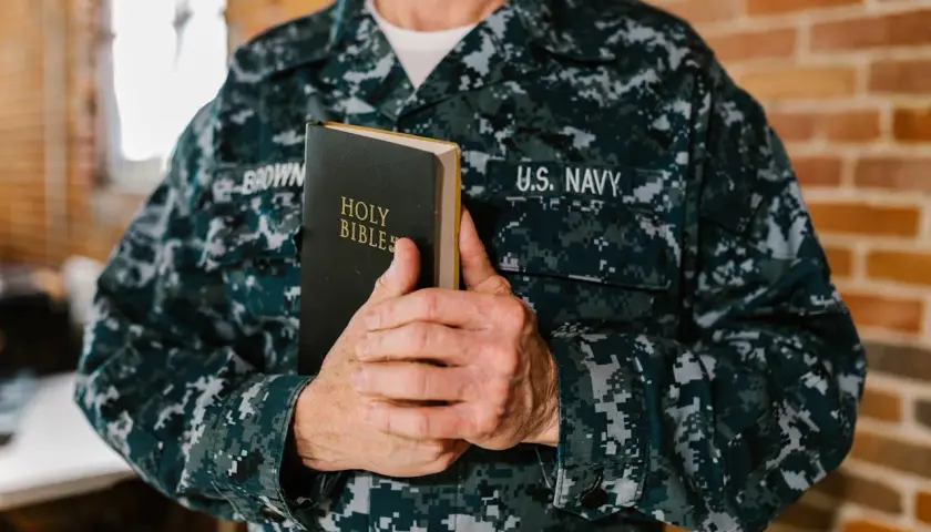 Marynarz w mundurze U.S. Navy trzyma Biblię. W jego dłoniach spoczywa księga, która może zawierać pieśń dawida, symbol wiary i nadziei.