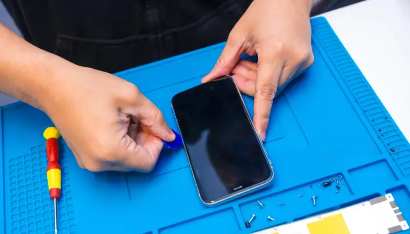 Ręce otwierają telefon, by włączyć nawigację. Obok leży śrubokręt i małe śrubki.