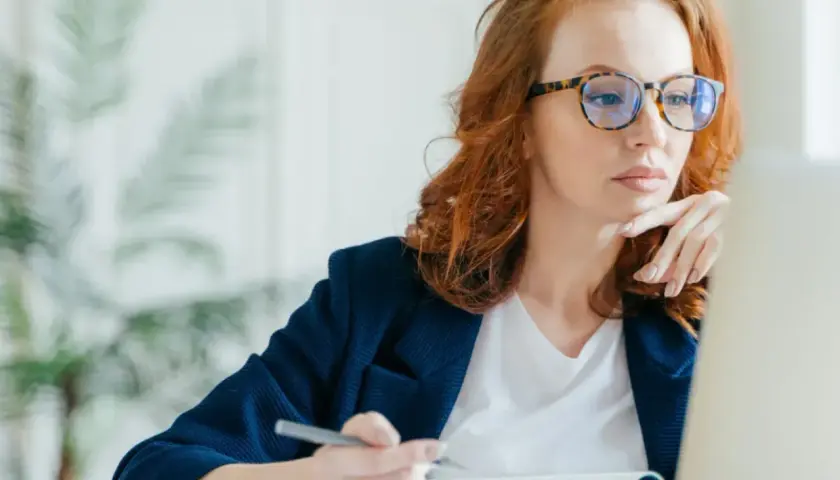 Kobieta w okularach z modną oprawką pracuje przy laptopie. Dofinansowanie do okularów może pomóc w zakupie stylowych i wygodnych oprawek.