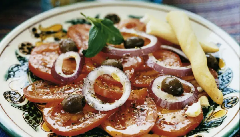 En läcker italiensk potatissallad med tomater, rödlök, oliver och basilika, serverad med grissini.