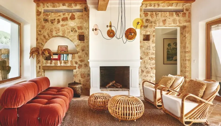 Gemütliches Wohnzimmer im Boho-Stil mit Terrakotta-Boden, Steinwand, Korbmöbeln und einem roten Samtsofa. Die boho bedeutung zeigt sich in der entspannten Atmosphäre.