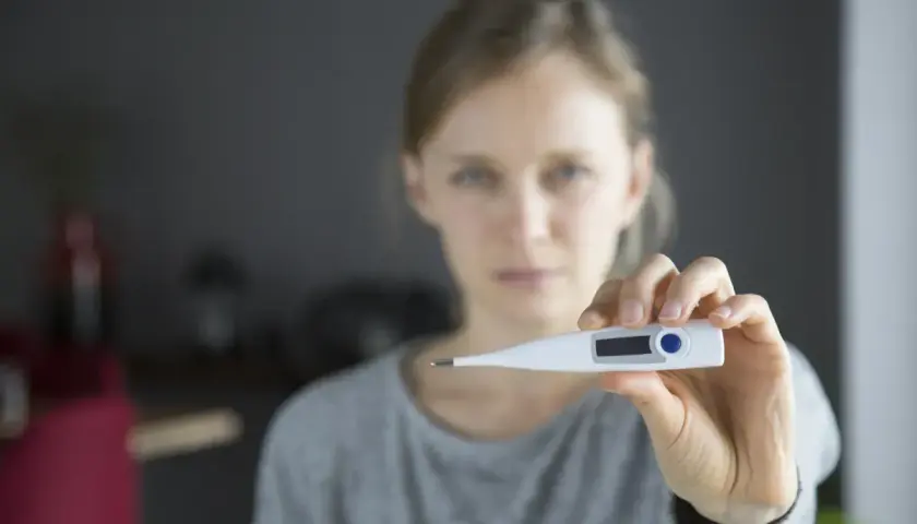 Kobieta trzyma termometr cyfrowy, wskazujący na podwyższoną temperaturę.