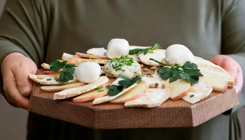 Carpaccio z selera z kulkami mozzarelli, jabłkiem i pastą ziołową na drewnianej desce.