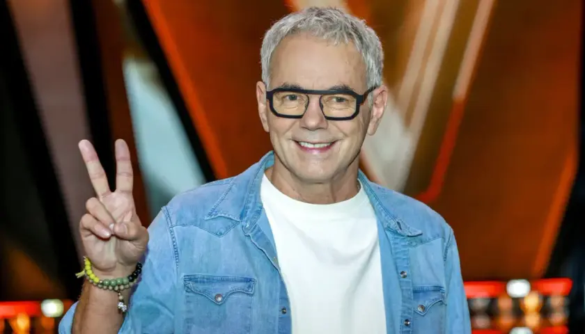 Robert Janowski, syn księdza, w dżinsowej koszuli i okularach, pokazuje znak pokoju.