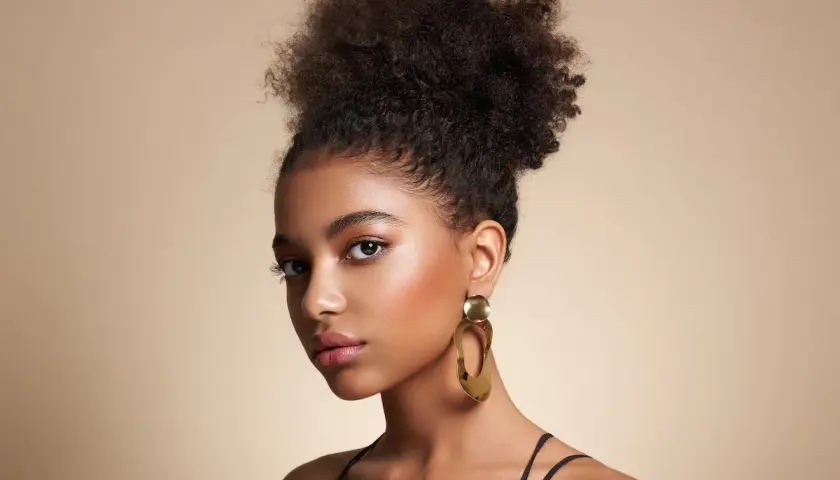 Joven con peinado afro y grandes pendientes dorados, luciendo unos estilos de maquillaje que realzan su belleza natural.