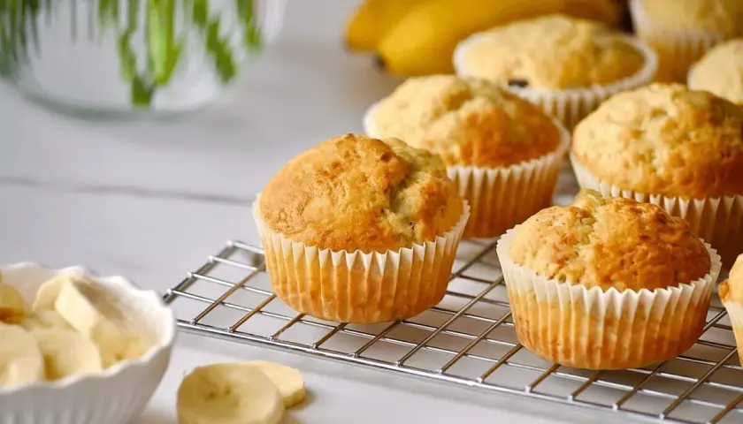 Frisch gebackene bananen muffins auf einem Gitter, daneben eine Schüssel mit Bananenscheiben.