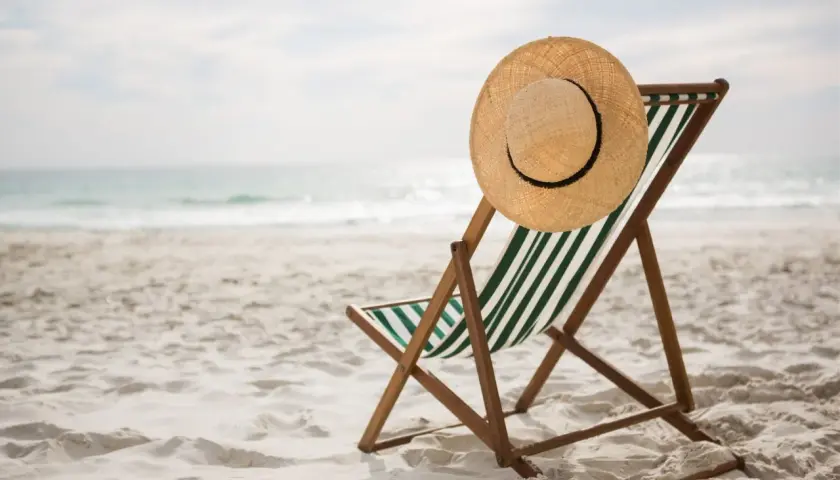 Leżak plażowy z kapeluszem na oparciu, gotowy na wczasy pod gruszą. Piasek, morze i słońce czekają.