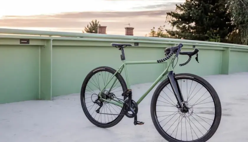 Zielony rower gravel z szerokimi oponami i pedałami platformowymi, idealny do odkrywania różnych rodzajów terenu.