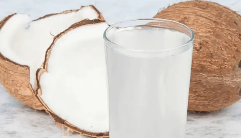 Ein Glas erfrischendes Kokoswasser steht neben einer aufgeschnittenen Kokosnuss. Kokoswasser gesund und lecker!