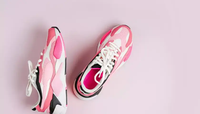 Różowe i białe buty sportowe, które wyglądają jak najszybsze buty do biegania, leżą na jasnoróżowym tle.