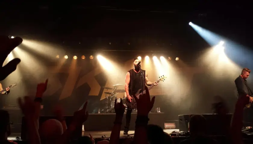 Koncert jednego z najsłynniejszych zespołów rockowych. Wokalista z basem na scenie, tłum szaleje.