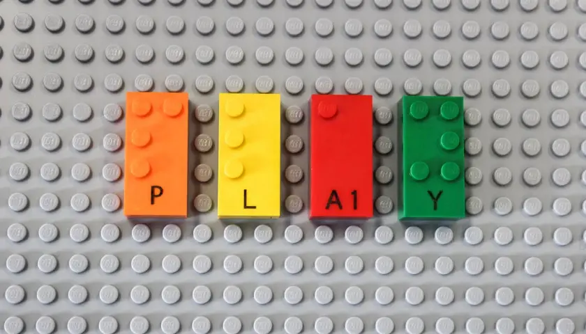 Vier bunte LEGO-Steine bilden das Wort "PLAY". Die Steine sind orange, gelb, rot und grün. Das Erkennen von LEGO-Steinen ist der erste Schritt zum Bauen.