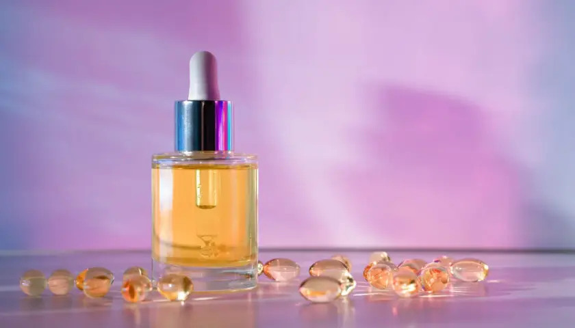 Szklana buteleczka z serum i kapsułki, które mogą zawierać retinol lub retinal, na tle fioletowo-różowego gradientu.