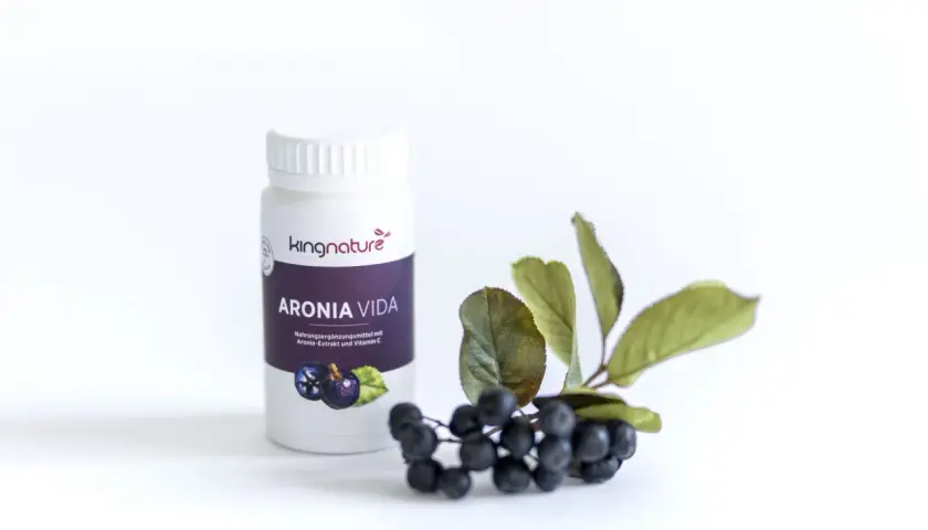 Flasche "ARONIA VIDA" mit Aronia-Extrakt und Vitamin C, daneben frische Aroniabeeren mit Blättern.