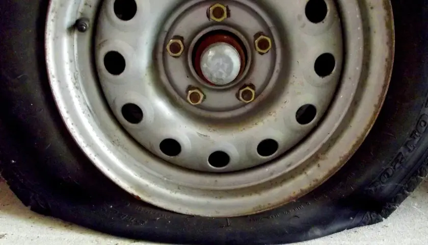Un clavo en rueda coche ha causado un pinchazo. La llanta metálica y el neumático desinflado se ven sobre el suelo de cemento.