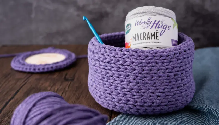 Ein lila gehäkelter Korb mit Garnrolle und Häkelnadel. Perfekt für eine makramee korb anleitung.