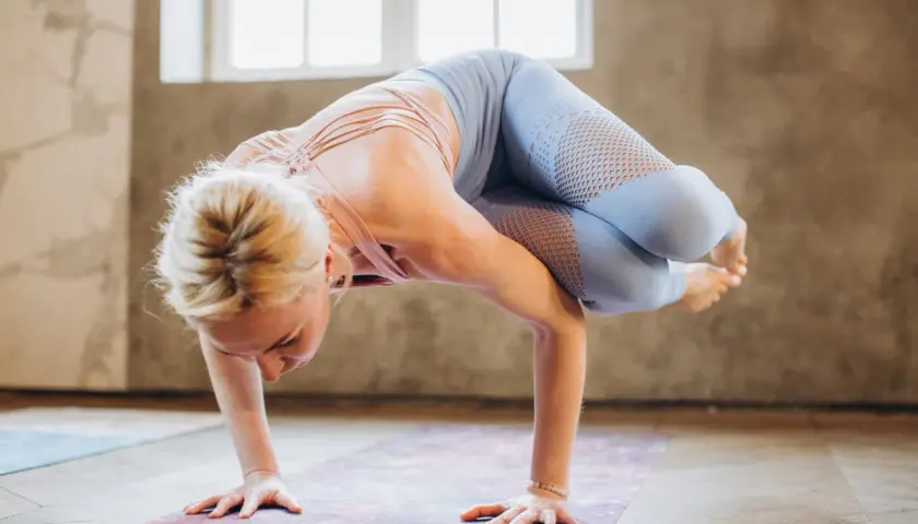 Woman in light blue yoga pants with mesh inserts balances in a challenging pose on a yoga mat.