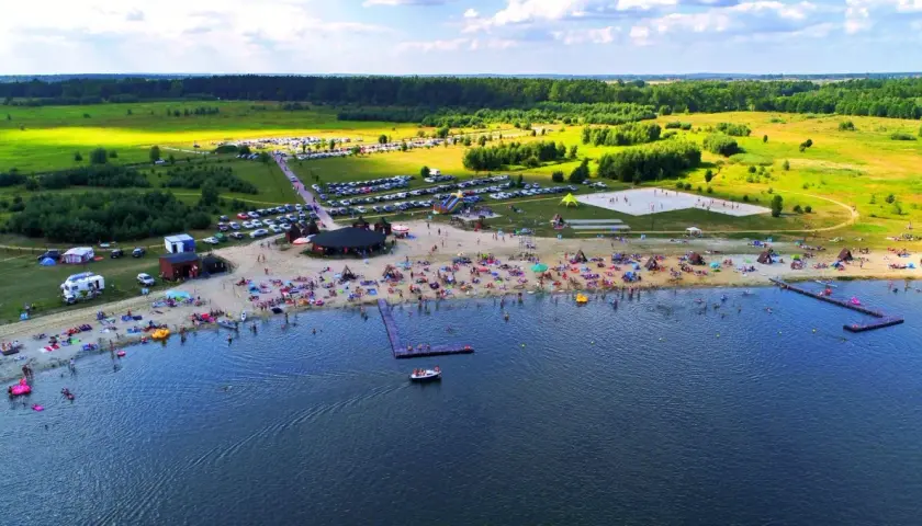 Tętniące życiem jeziora na Dolnym Śląsku latem. Plaża pełna ludzi, namioty, parkingi i zieleń wokół.