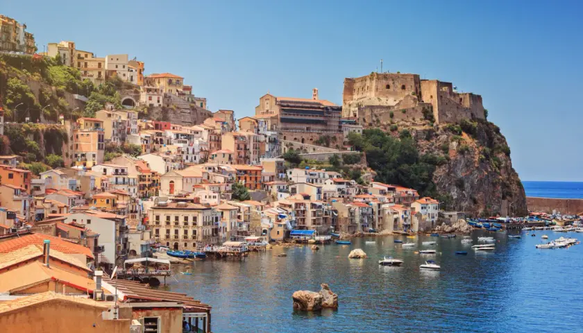 Colorful houses cascade down a cliffside to a harbor filled with boats, overlooking the sea. This is one of the picturesque cities in Calabria, Italy.