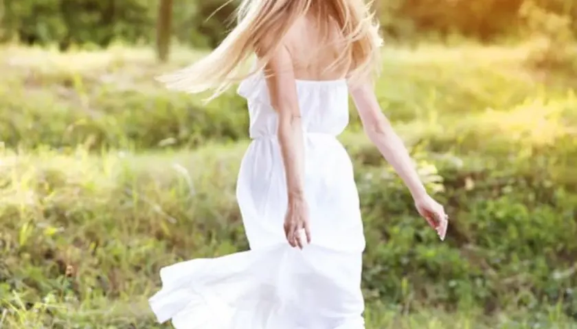 Une jeune femme aux cheveux blonds, portant une couronne de fleurs et une robe blanche légère, incarne l'esprit du printemps. Elle danse dans un champ verdoyant, une vision parfaite pour savoir comment s'habiller au printemps.