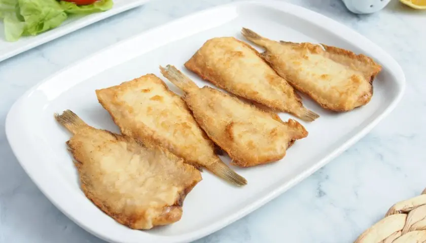 Cinco acedias fritas doradas y crujientes en un plato blanco, listas para disfrutar.