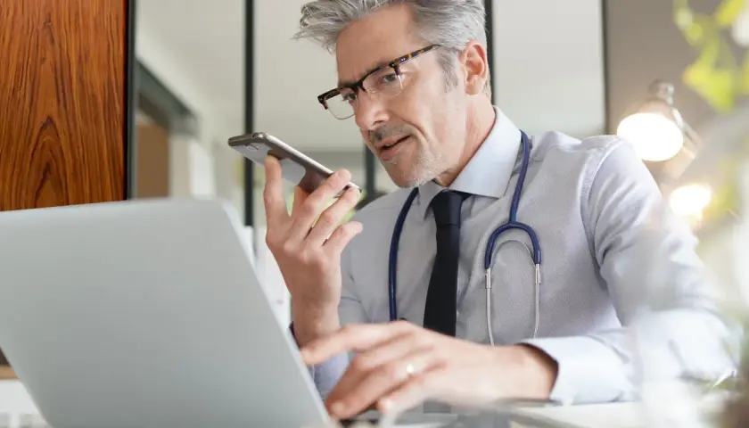 Lekarz w okularach rozmawia przez telefon, pracując przy laptopie.