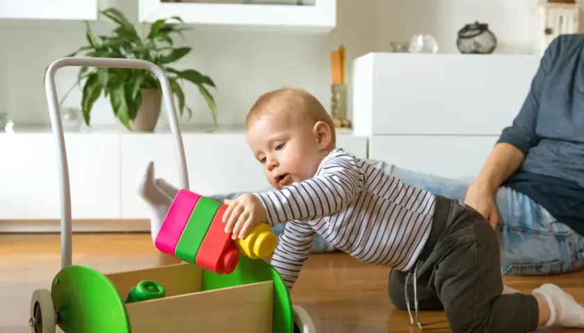 8 miesięczne dziecko raczkuje i bawi się kolorowymi klockami w drewnianym wózku.