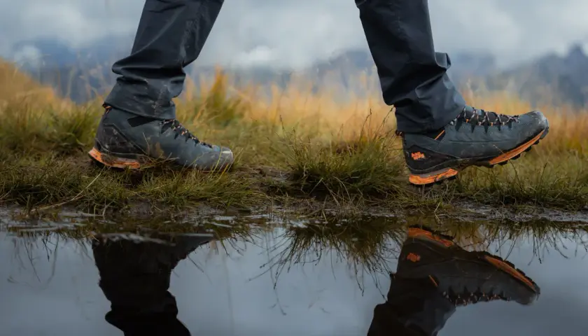 Hiking boots reflected in a puddle. Learn how to get your shoes to stop squeaking on your next adventure.