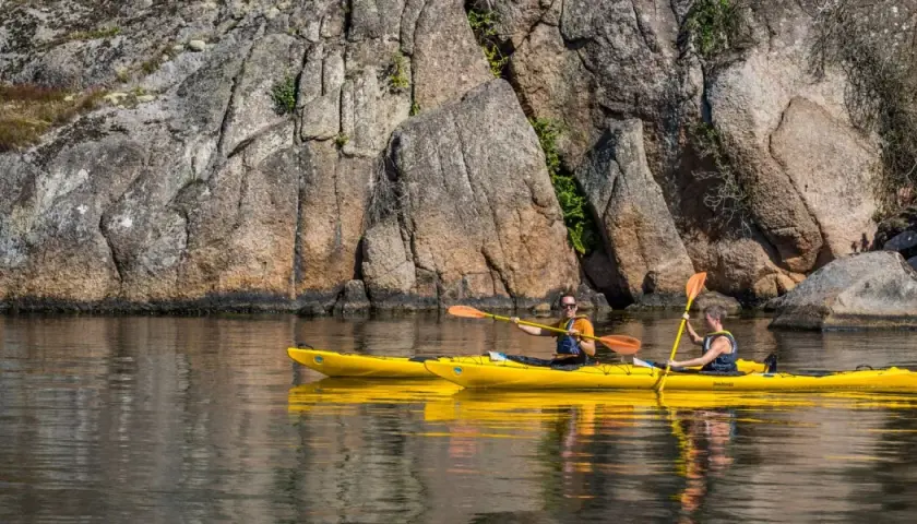 Två personer paddlar varsin gul kajak längs en klippig kust. En härlig dag för upplevelser i Sverige.