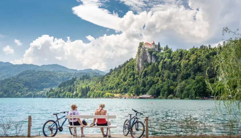 Para odpoczywa na ławce, podziwiając zamek na skale nad jeziorem Bled. Idealne miejsce na camping Bled Slovenia.