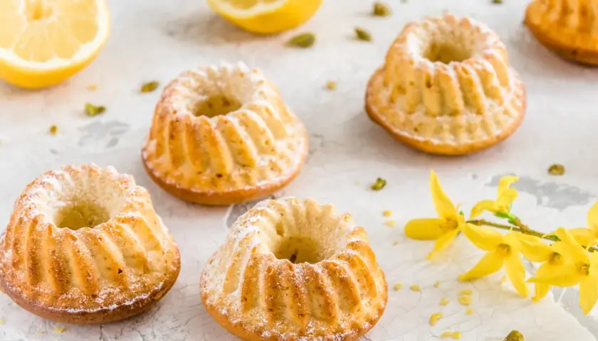 Szybkie babeczki wielkanocne z cytryną i pistacjami, ozdobione cukrem pudrem i gałązką forsycji.