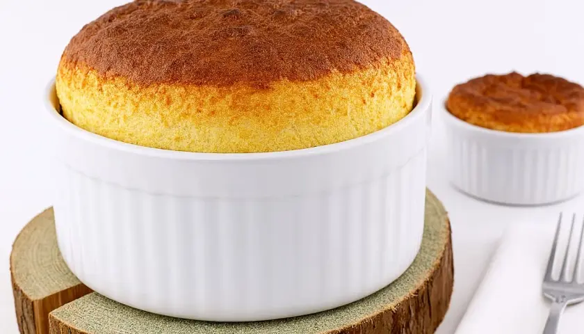 Deux soufflés au fromage dorés, prêts après leur temps de cuisson. L'un est dans un grand ramequin blanc, l'autre dans un plus petit.