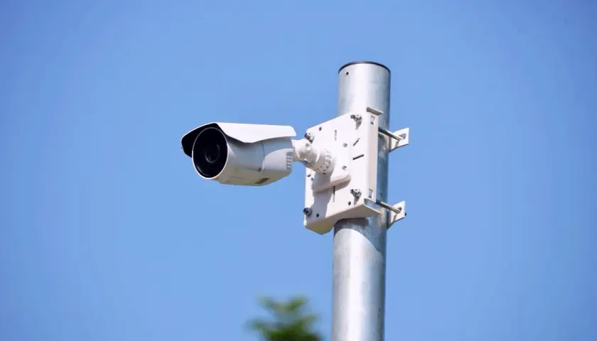 Biała kamera zewnętrzna zamontowana na metalowym słupku, idealna do monitorowania otoczenia. Dowiedz się, jak zamontować kamerę zewnętrzną.