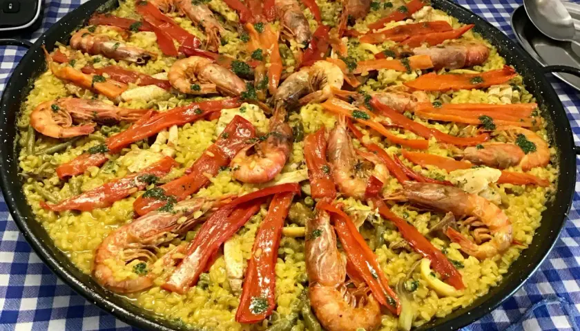 Paella mar y montaña, un festín de arroz amarillo con gambas, pimientos rojos y verduras.