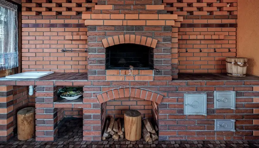 Solidny, murowany prosty grill z cegły, gotowy na letnie przyjęcia. Obok zlew i drewniana beczka.