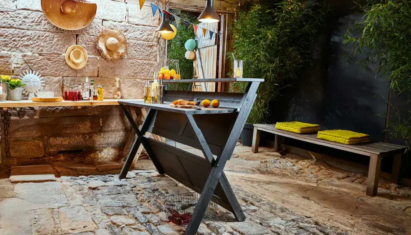 Rustikale Bar selber bauen: Eine dunkle Holzbar mit Orangen und Getränken, dekoriert mit bunten Wimpeln und Hüten. Perfekt für Gartenpartys.