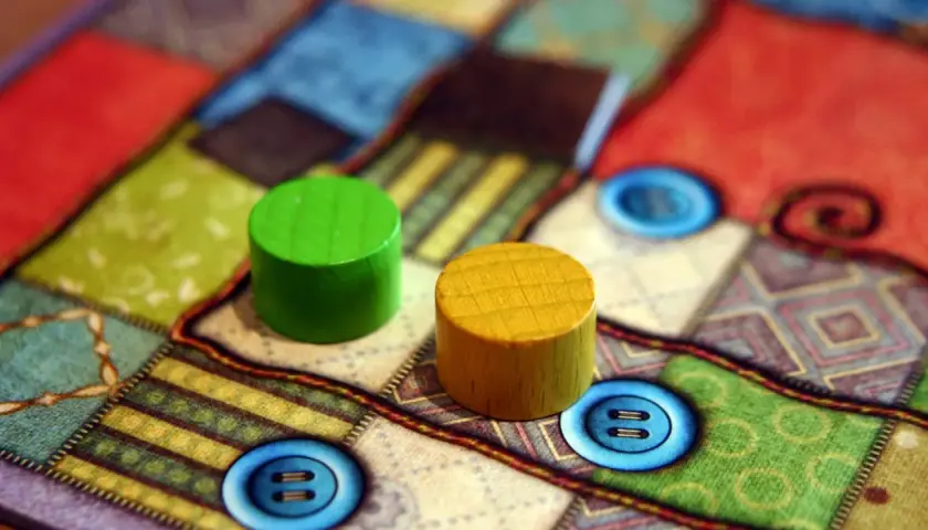 Zwei Holzfiguren auf einem bunten Brettspiel mit Knopf-Symbolen. Perfekt für die besten 2 Spieler Brettspiele.