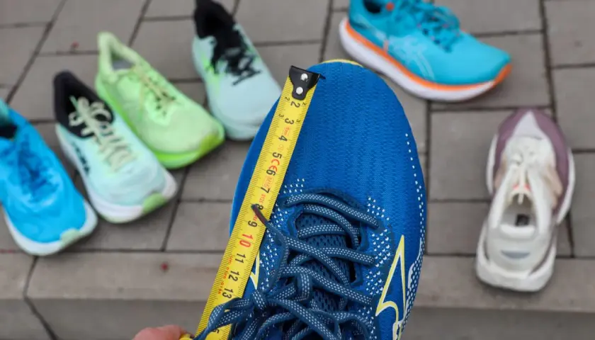 Miarka mierzy niebieskie buty do biegania. Czy buty do biegania powinny być większe? W tle inne kolorowe buty.